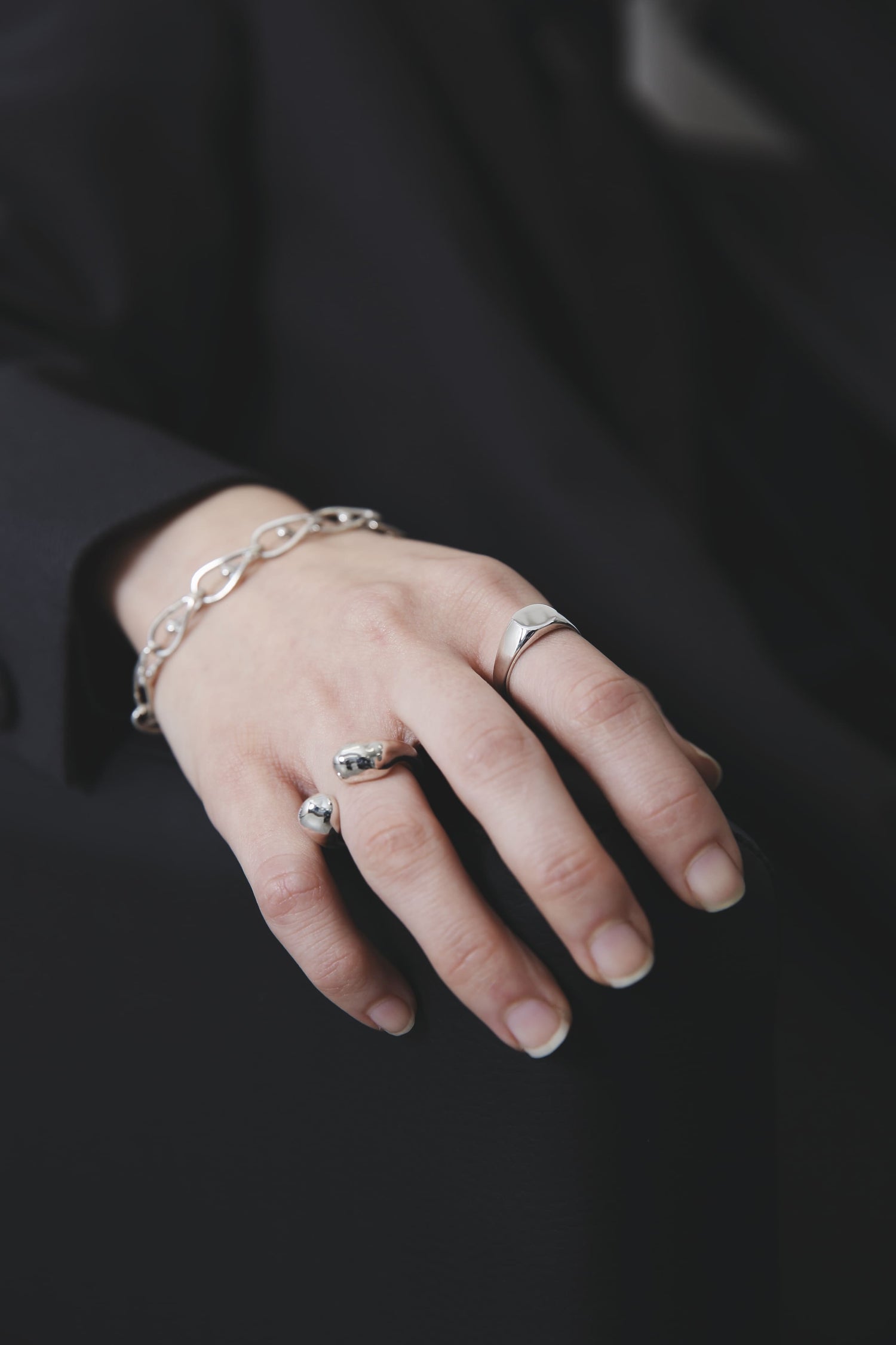 黒いジャケットの袖から覗く手元のアップ。シルバーの輝きが際立ち、リングとブレスレットの組み合わせが洗練された印象を与える。