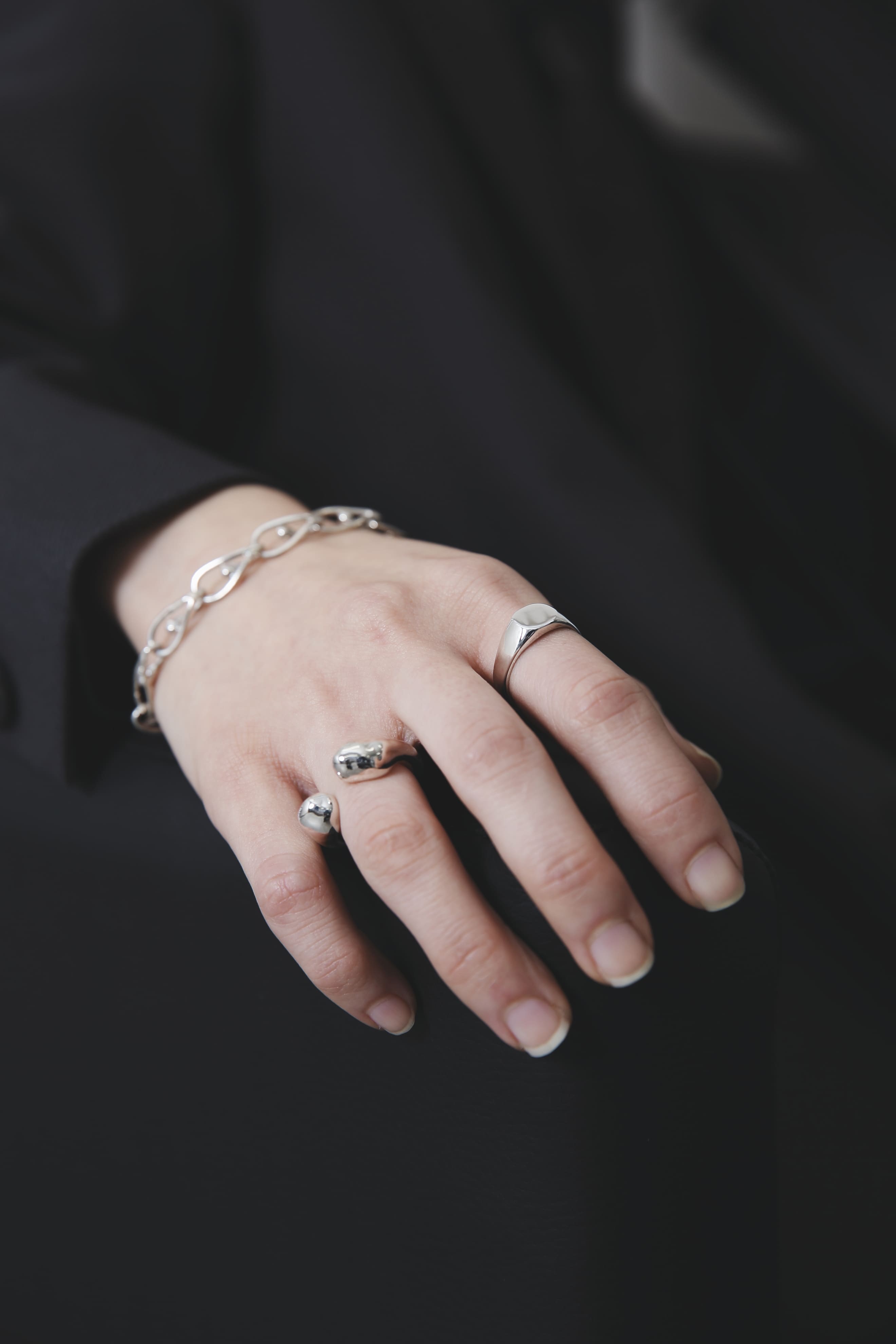 黒いジャケットの袖から覗く手元のアップ。シルバーの輝きが際立ち、リングとブレスレットの組み合わせが洗練された印象を与える。