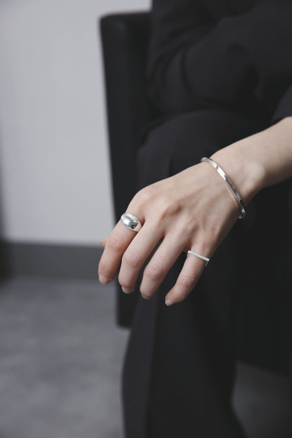 同デザインのリングを身につけ、腕を抱くように組んだショット。無駄のないデザインが際立ち、ミニマルでジェンダーレスな雰囲気を漂わせる。