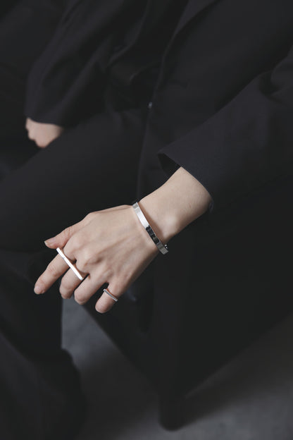 膝に手を添え、鏡面仕上げのシルバーバングルとロングバーデザインのリングを着用したスタイリングカット。黒の装いに映えるシャープなシルバーの輝き