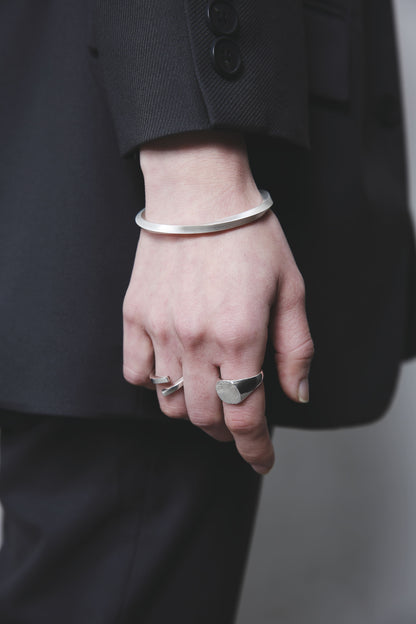 黒いジャケットの袖口から覗くシルバーバングルと、木目模様のシルバーリング。直線的なフォルムと滑らかな光沢がスタイリッシュな印象を与える。