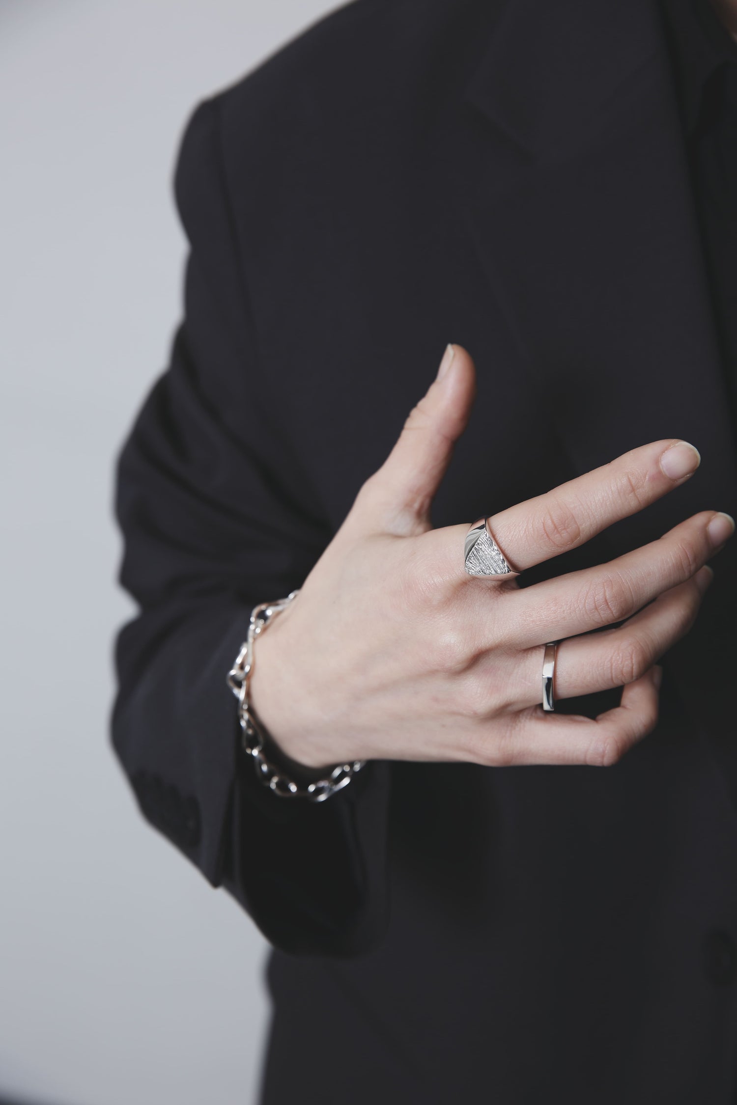 両手で三角形の木目シグネットリングを指にはめる仕草。光沢感のあるリングと、滑らかに繋がるチェーンブレスレットが上品な印象を与える。
