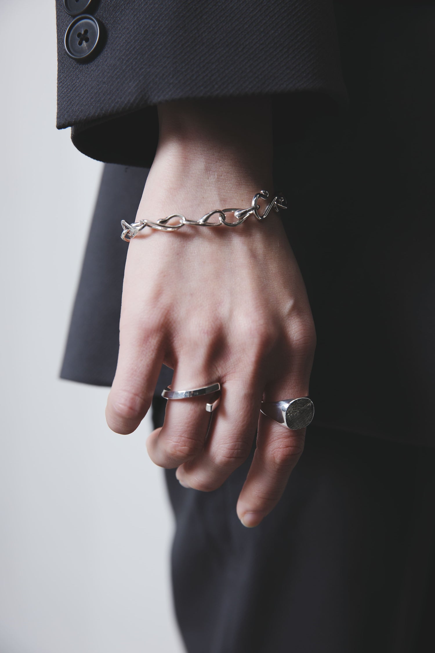 チェーンリンクデザインのシルバーブレスレットと、質感の異なる2つのシルバーリングを重ね付けした手元。丸いトップの木目模様リングが印象的で、ミニマルながら個性を感じるスタイル。