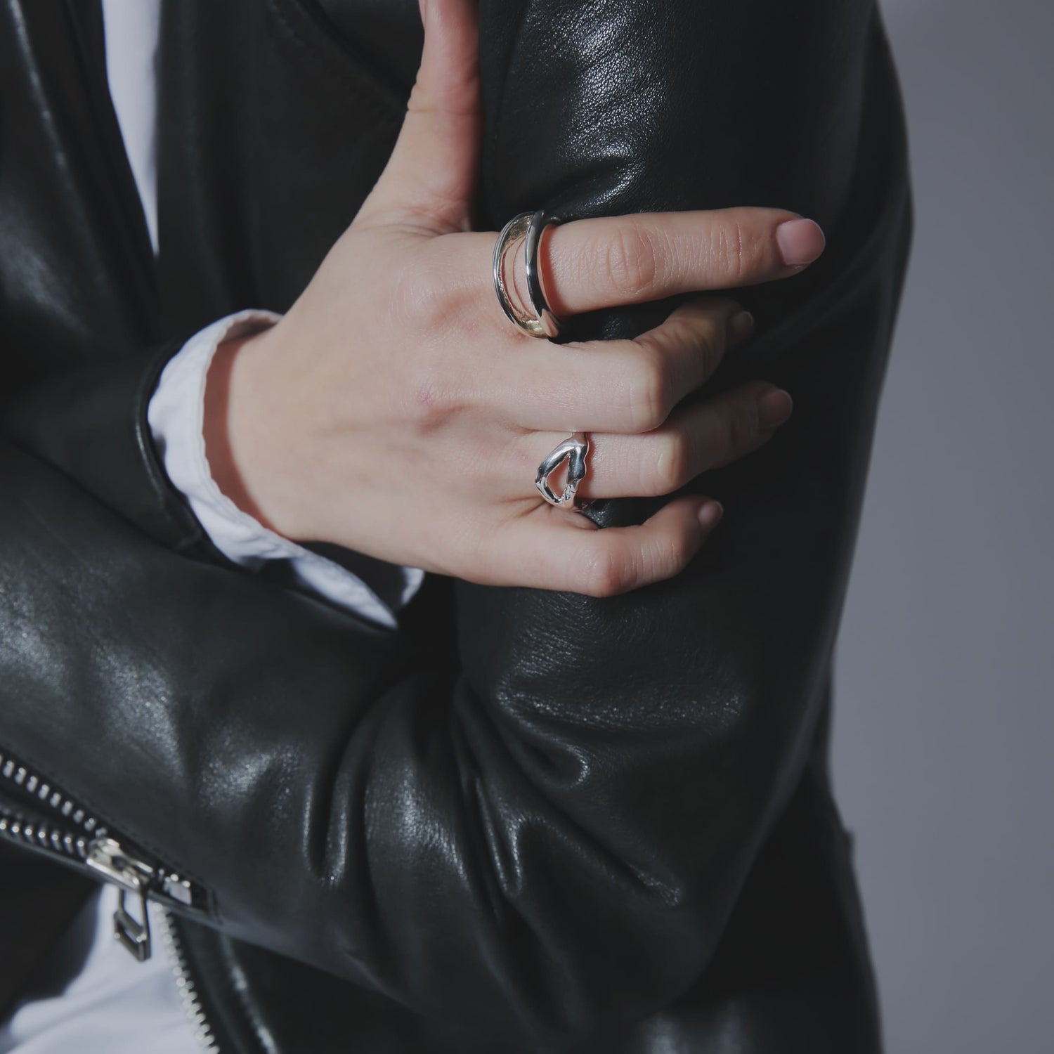 黒のレザージャケットを羽織り、シルバー925製のリングを人差し指と薬指に重ね付けしたスタイリング。ハードな素材感にシルバーの光沢が映える手元のアップ。