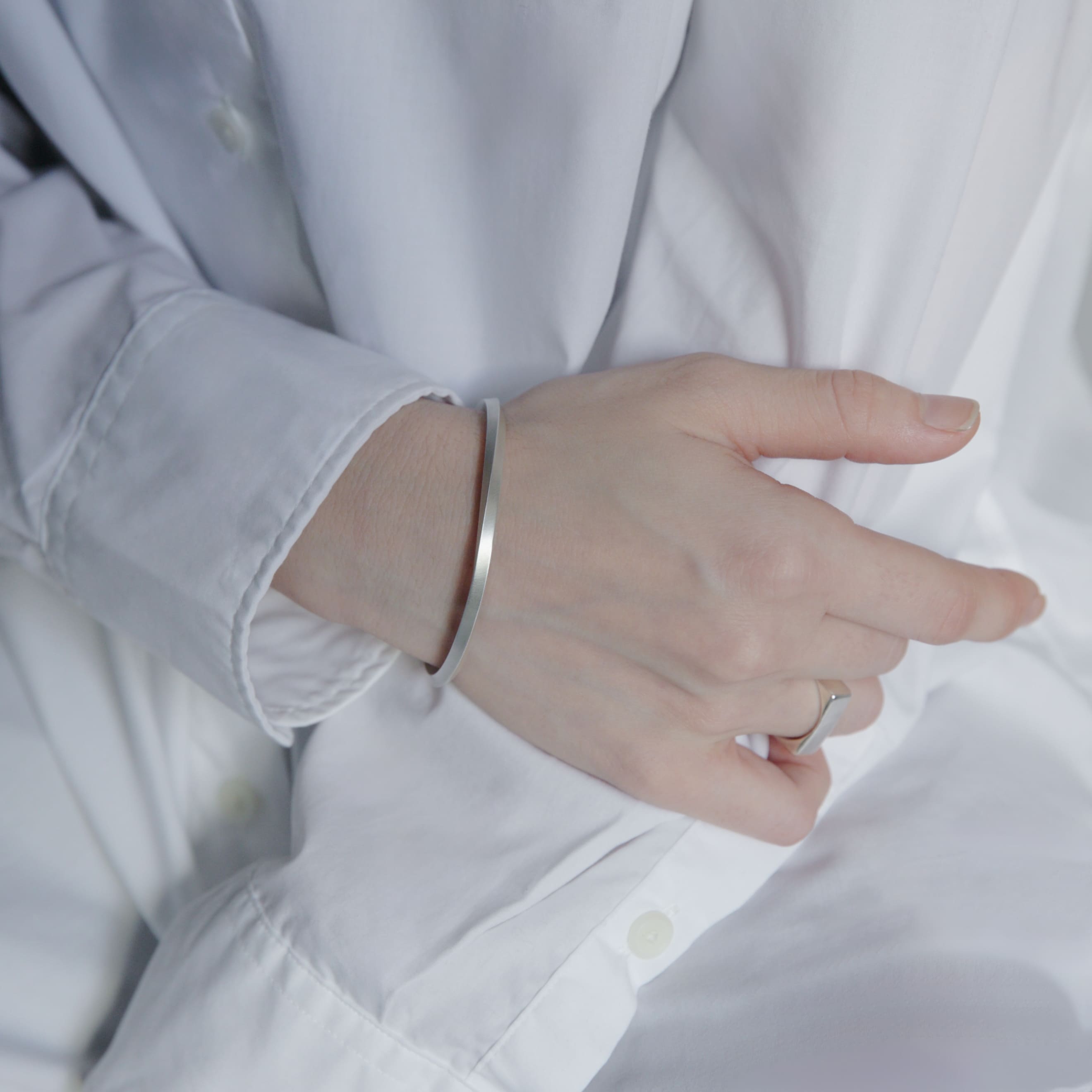 白いシャツの袖口からのぞくシルバーバングルの着用写真。ミニマルな細身デザインが手元にさりげない存在感を与える。