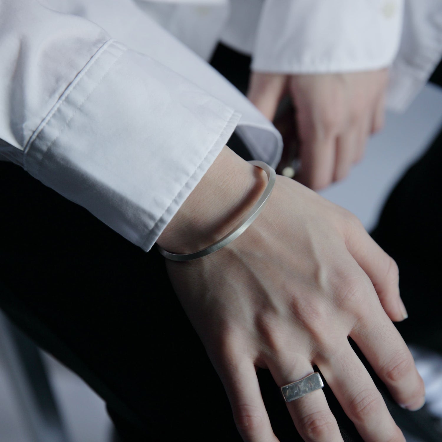 ブラックのボトムスと合わせた手元に、マットシルバーのバングルとリングをコーディネートした着用イメージ。直線的なフォルムが印象的。