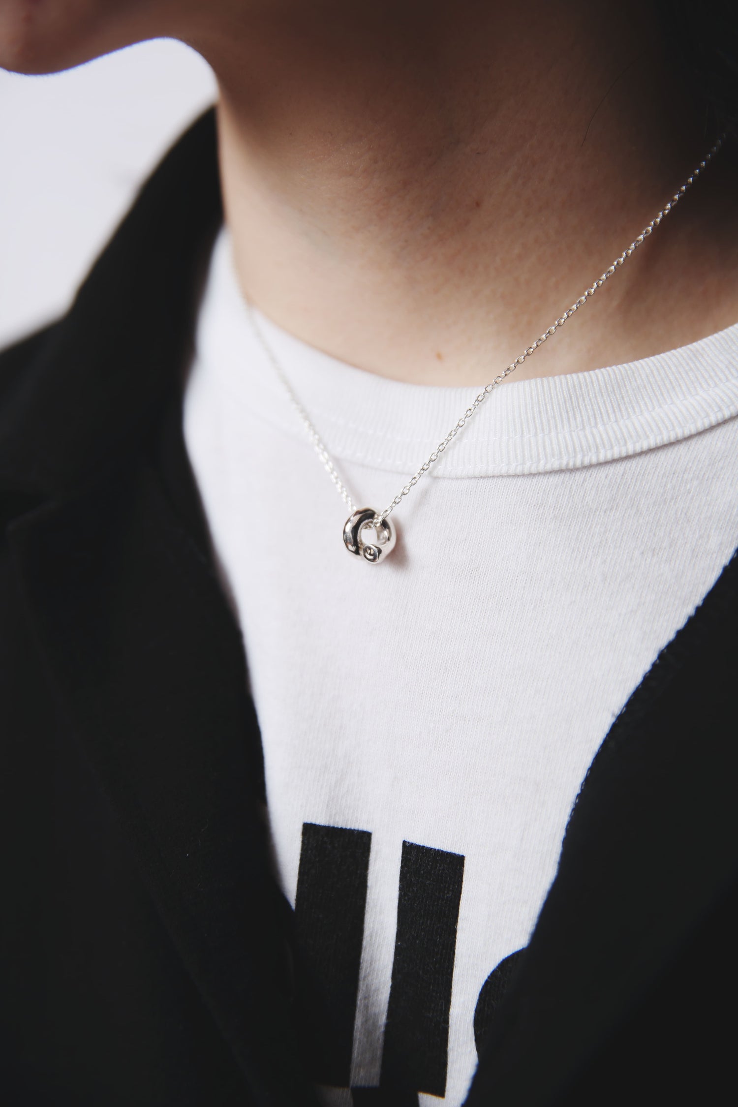 白いTシャツとブラックジャケットの上に輝く、シルバー925製のにこちゃんの顔つきペンダントネックレス。小ぶりながら存在感のあるフォルムが首元を引き締める。