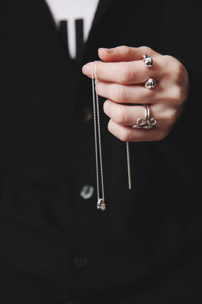 手に持たれたシルバー925のペンダントネックレス。滑らかな曲線が交わる立体的なデザインが特徴で、モードな印象を添える。