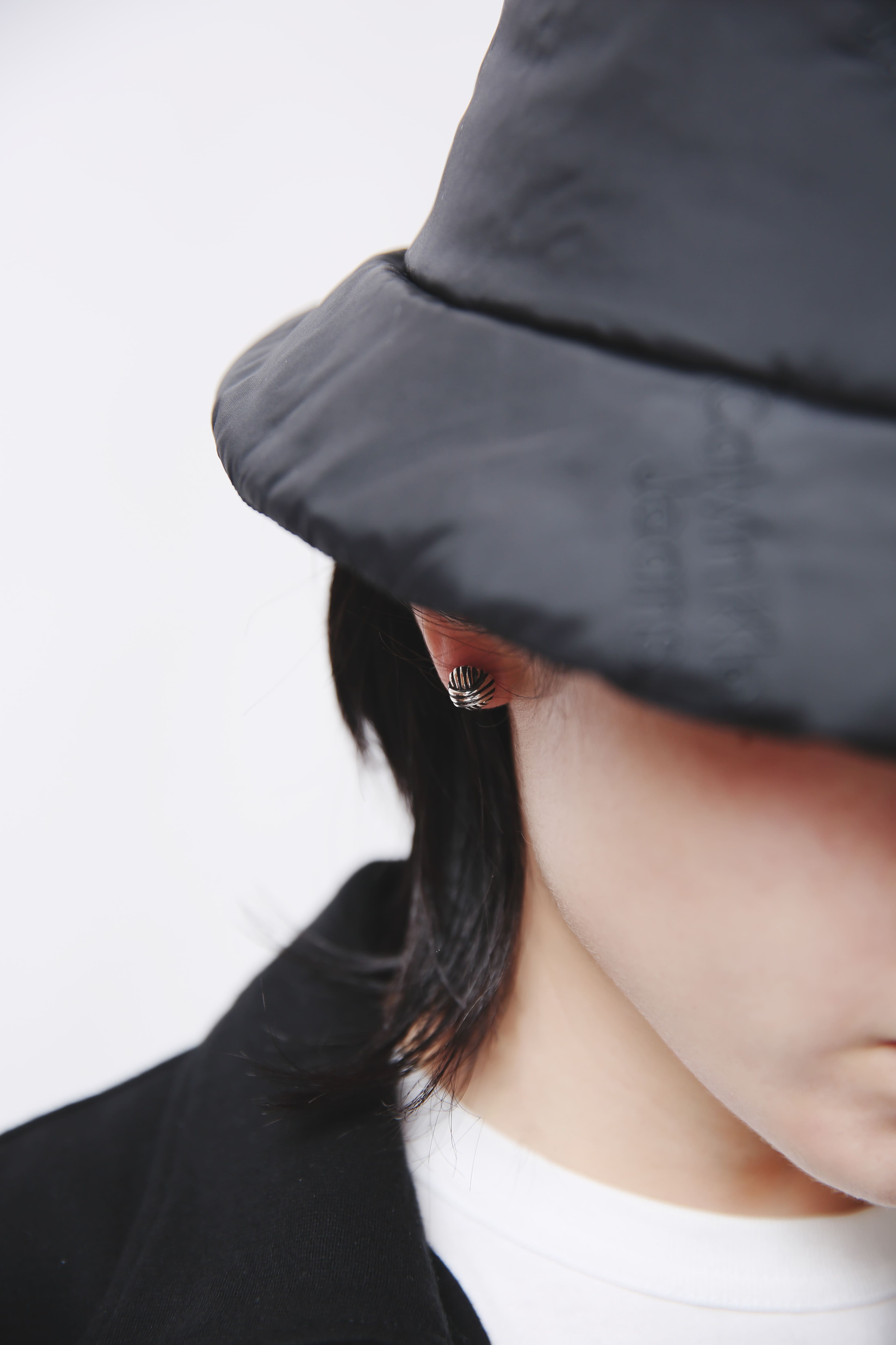 Nine Nineの「ロココピアス」を黒のバケットハットとモノトーンコーデに合わせた着用イメージ。ロココ時代のボタン装飾をモチーフにしたシルバー925ピアス。