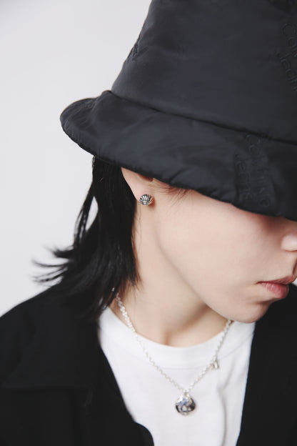 Nine Nineの「ロココピアス」を黒のバケットハットとモノトーンコーデに合わせた着用イメージ。ロココ時代のボタン装飾をモチーフにしたシルバー925ピアス。