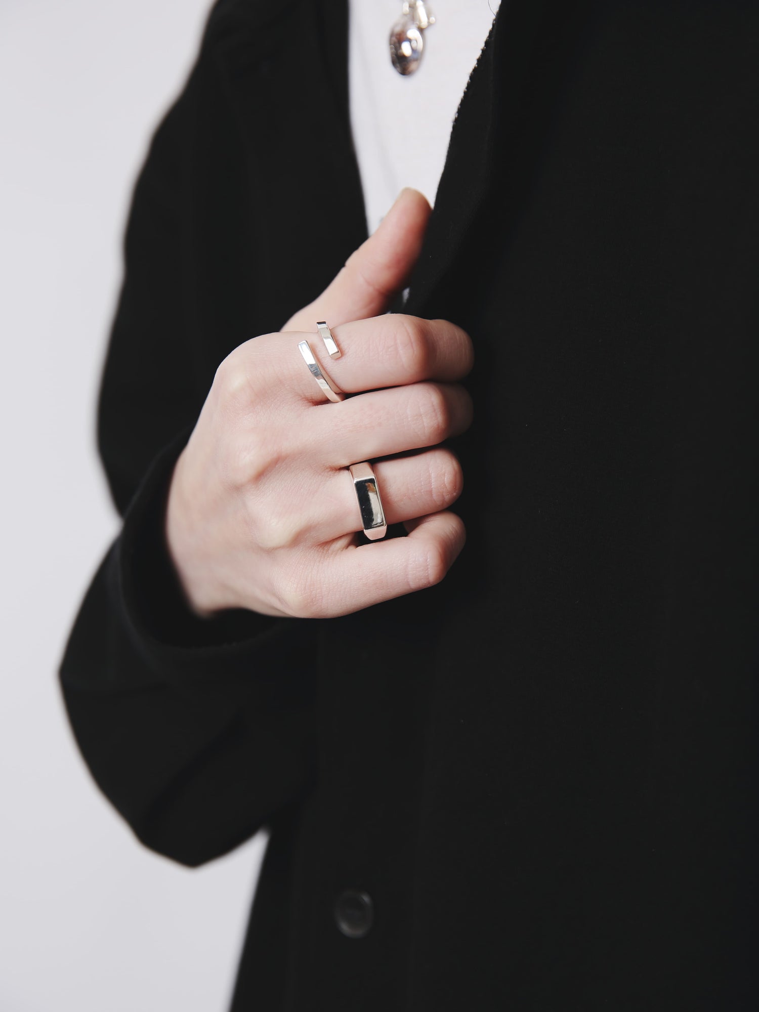 黒いコートの胸元に映えるシルバーリング。直線的なラインが特徴のデザインと、黒いスクエアトップのリングを重ね付けし、モードな雰囲気を演出している。