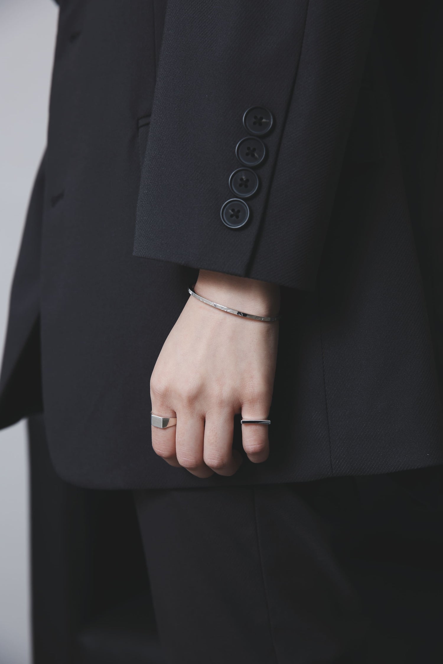 黒のジャケットから覗く手首に、槌目模様の入ったシルバー925製の細身バングルと、2本の異なる太さのリングを組み合わせた手元のスタイリング。