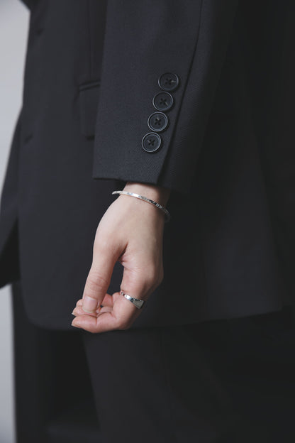 スーツの袖から覗く手元に、表面に凹凸のあるシルバー925製のバングルと、波打つフォルムのリングが印象的なシンプルで洗練された手元。