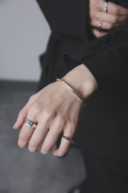 手の甲をやや前に出した構図で、バングルと2本のリングが光を受けて輝く。クラシックな黒の装いに、無駄のないシルバージュエリーが映えるカット。