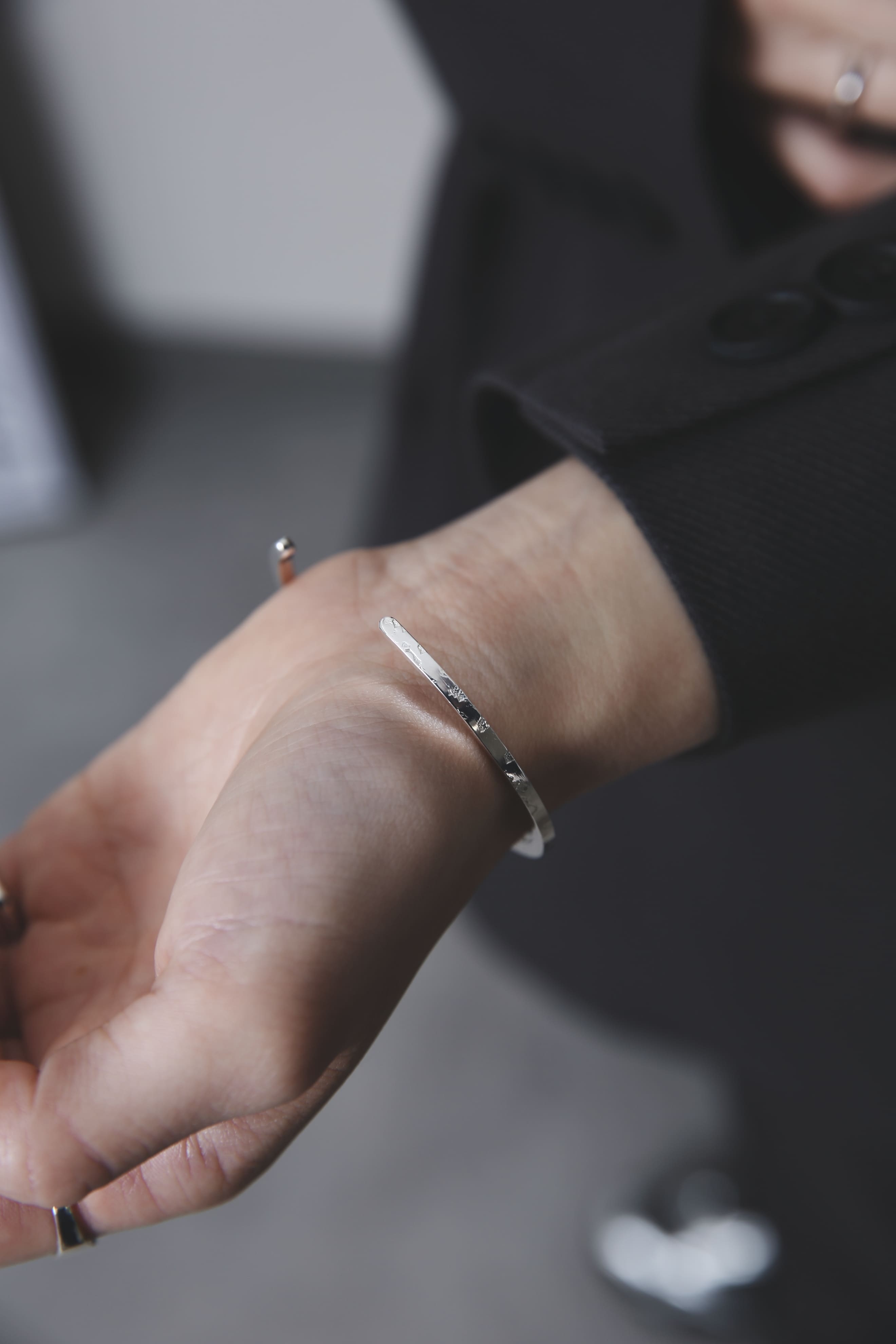 槌目模様が際立つシルバー925製バングルを着用した手元のアップ。光の中で素材の表情が引き立つ構図。