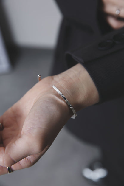 槌目模様が際立つシルバー925製バングルを着用した手元のアップ。光の中で素材の表情が引き立つ構図。