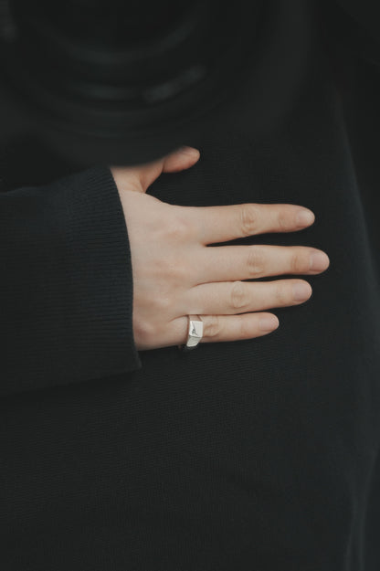 黒いトップスの袖口から覗く手元に、台形フォルムのシルバーシグネットリングを着用。無駄のないデザインが、落ち着いたスタイルの中で静かに輝きを放つ。