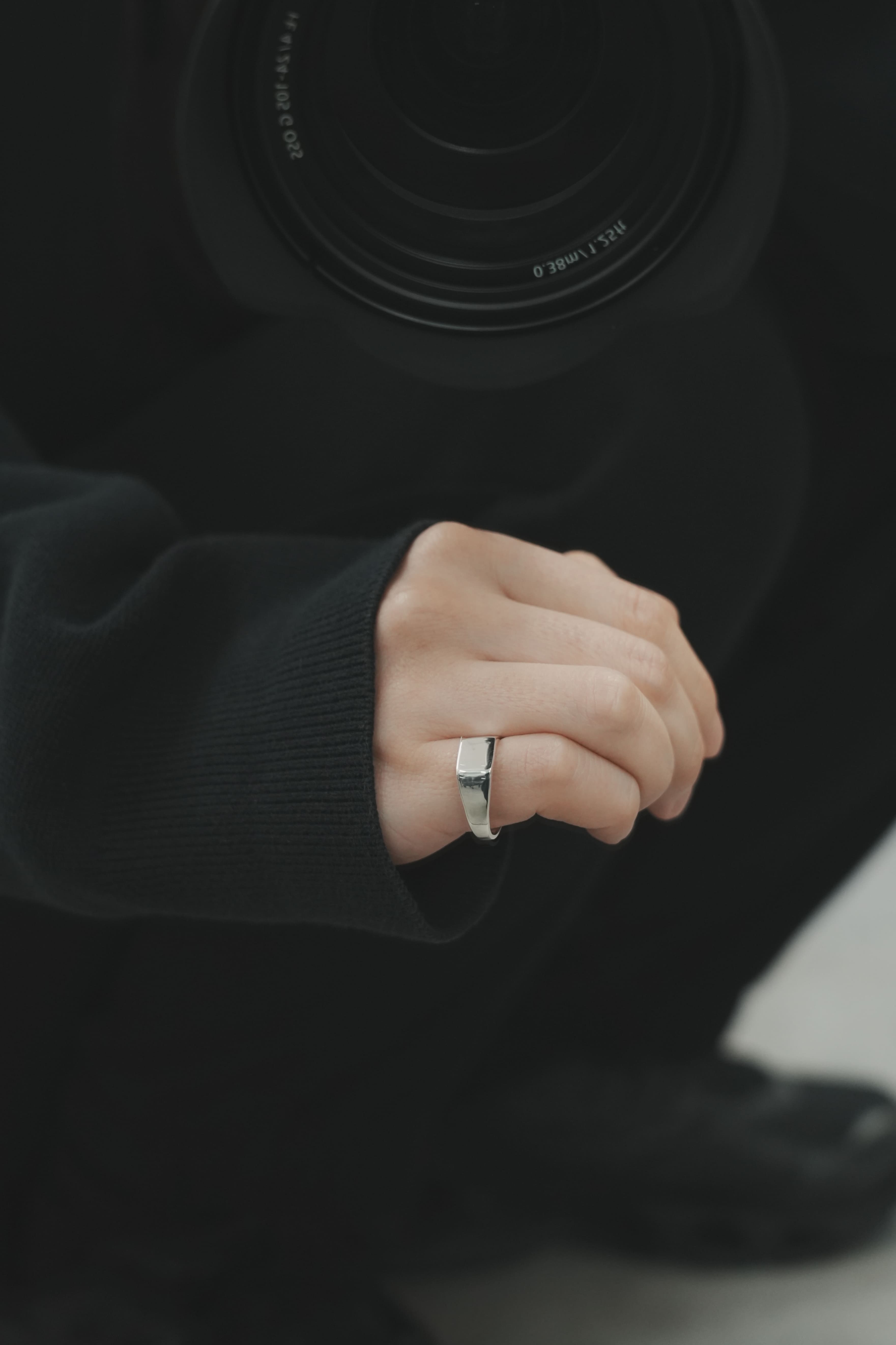 シャープなラインが特徴のシルバーシグネットリングを着用。マットな黒の服地と対照的な鏡面の輝きが、上品な存在感を際立たせている。
