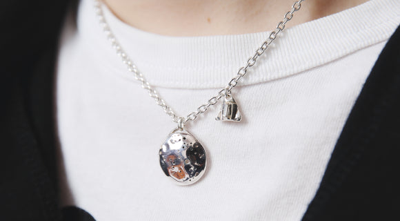 美しいシルバーペンダントと小さなチャームのネックレスを着けた胸元。
