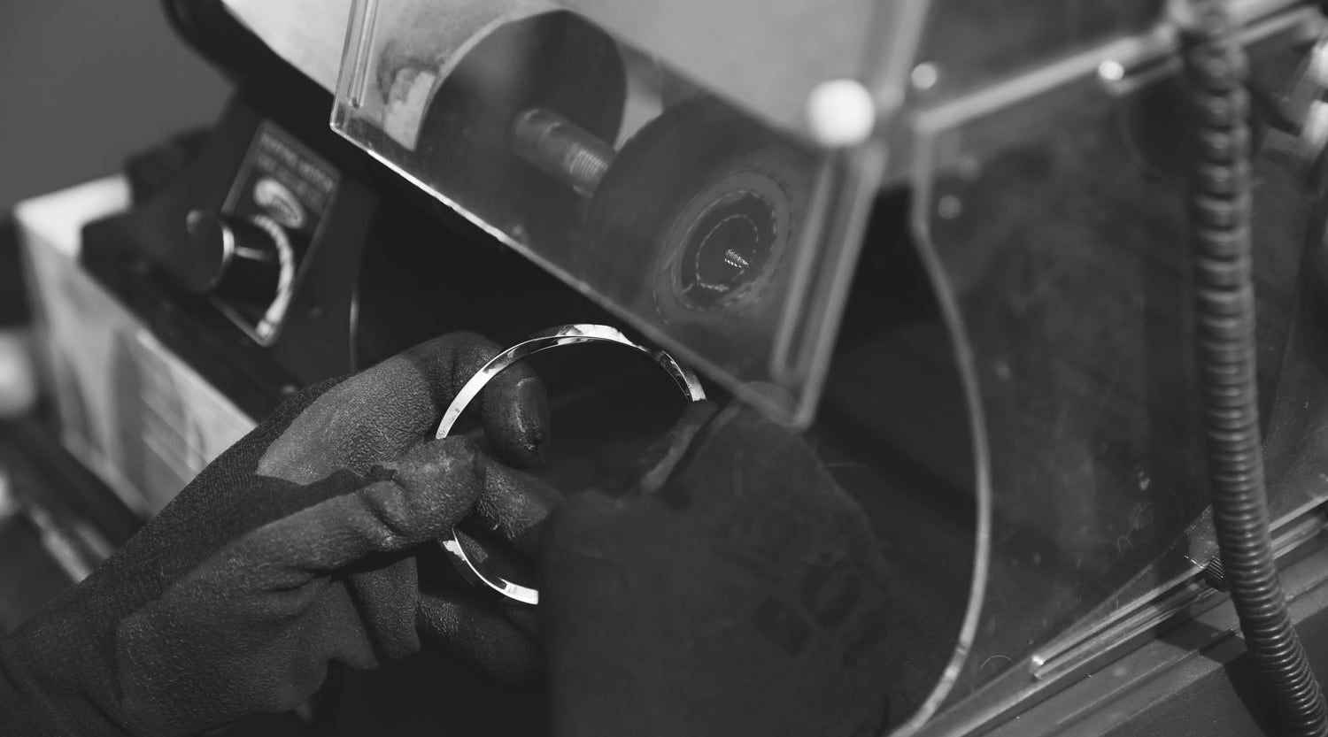 職人がグローブを着けてバングルを研磨している様子。磨き上げられたシルバーの表面が光を反射し、Nine Nineの丁寧なものづくりを感じさせる一枚。